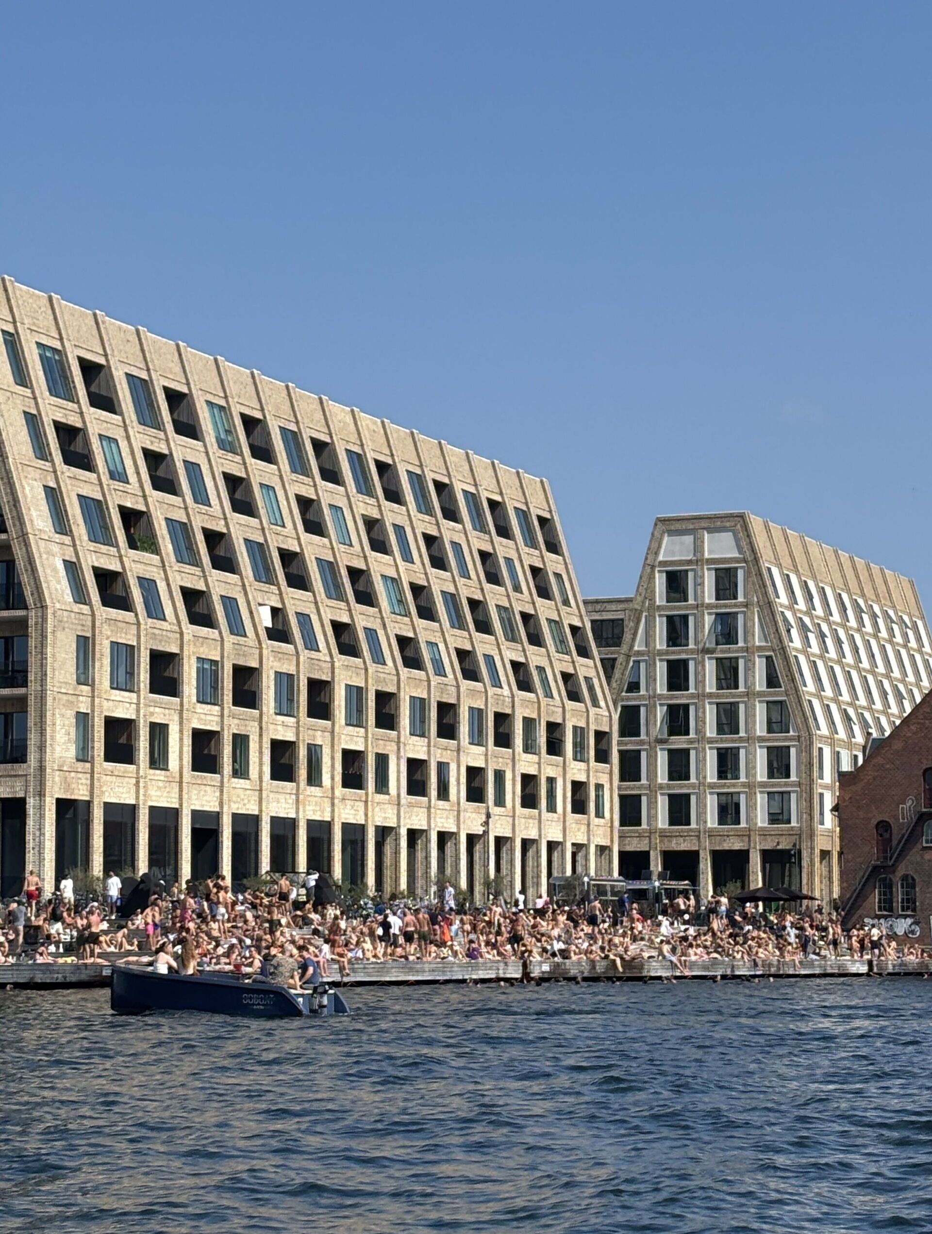 Ein Gebäude am Wasser mit einer rasterförmigen Fassade und einem geneigten Dach.