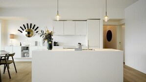 Et moderne køkken med en central ø, hvide skabe, hængende lamper og en dekorativ vægkunst.