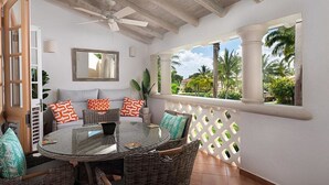 A covered patio with wicker furniture, a round glass table, and a ceiling fan.