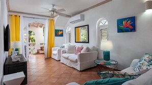 A living room with white sofas, a glass coffee table, and artwork on the walls.