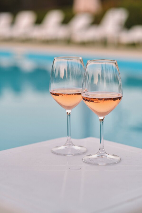 Two wine glasses on a white table by a pool.