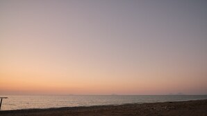 Ein Strand bei Sonnenuntergang, bewölkter Himmel und ruhige See.