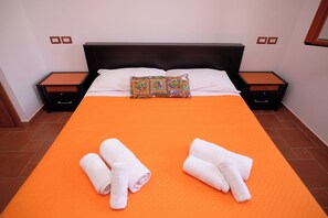 A neatly made bed with an orange bedspread, white pillows, and a colorful decorative pillow. There are two white towels folded on the bed. - Residence Costa Tirrena (Torrenova)