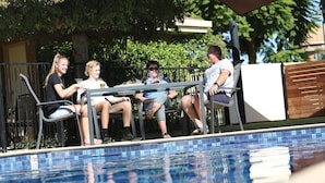 Eine Gruppe von Personen sitzt an einem Pool mit Metallgeländer und gefliestem Rand.