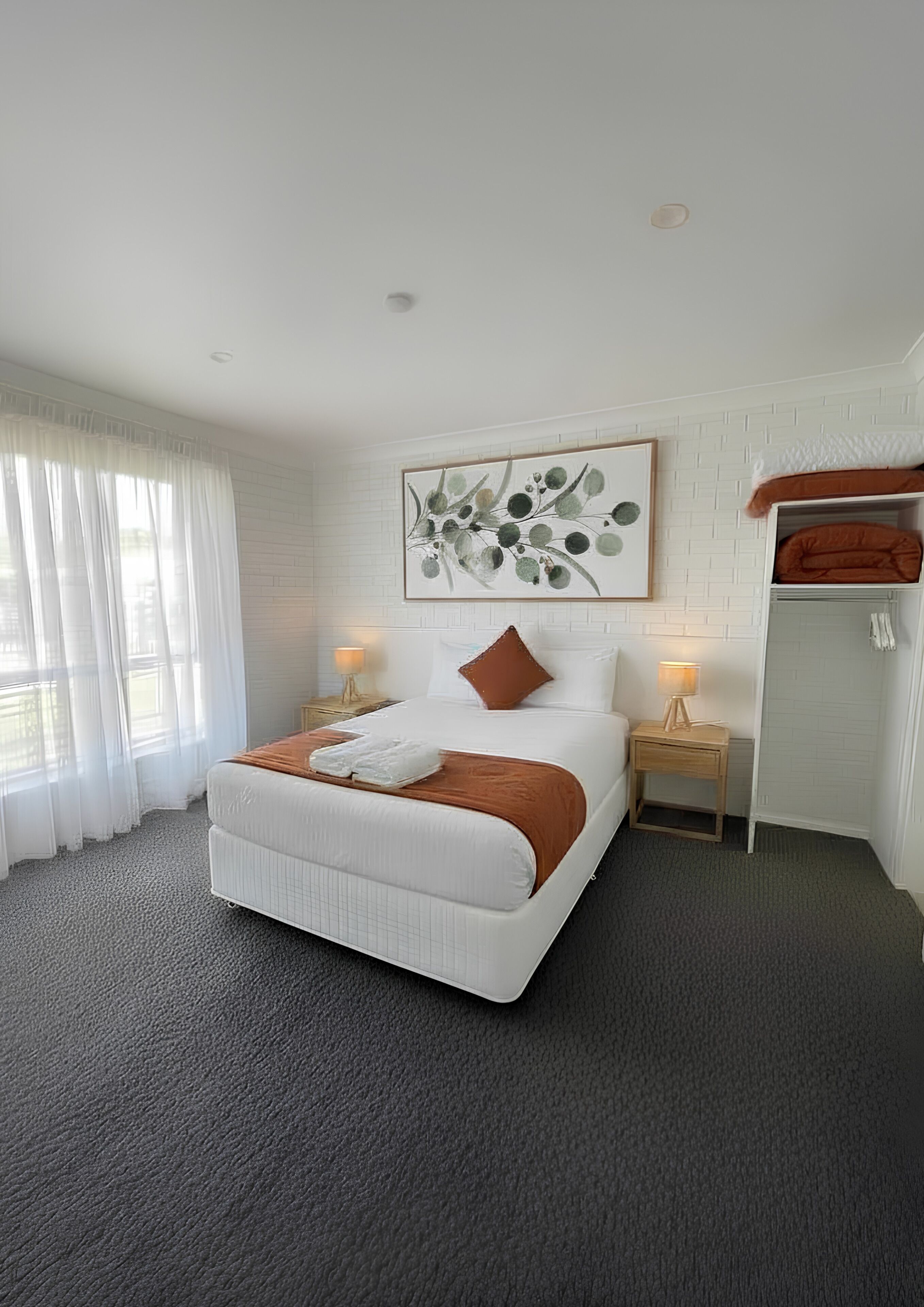 A modern bedroom with a large bed, a nightstand, a lamp, a wall-mounted artwork, and a bunk bed in the corner.