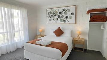 A modern bedroom with a large bed, a nightstand, a lamp, a wall-mounted artwork, and a bunk bed in the corner.