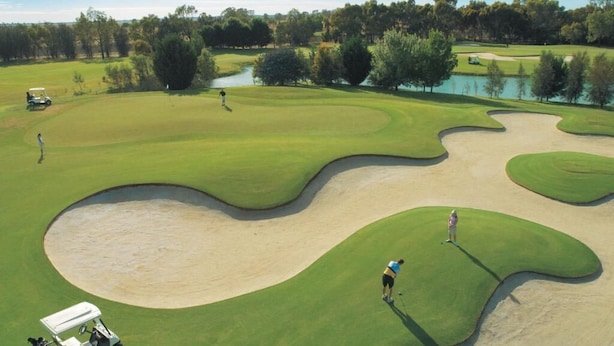 Ein Golfplatz mit Sandbunkern, einem Teich und Bäumen im Hintergrund.
