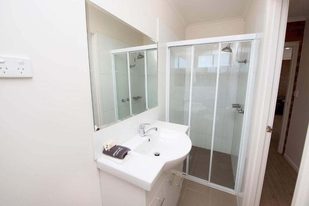 Un baño con un lavamanos blanco, cabina de ducha de vidrio y un espejo sobre el lavamanos.