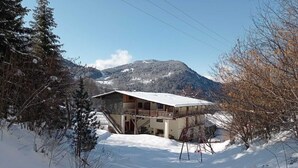 A snow-covered cabin with a wooden exterior, a balcony, and a staircase leading to the entrance. - Savoie, St François Longchamp, Très Grand Appartement de 180 m2, 12 Couchages (Saint-François-Longchamp)