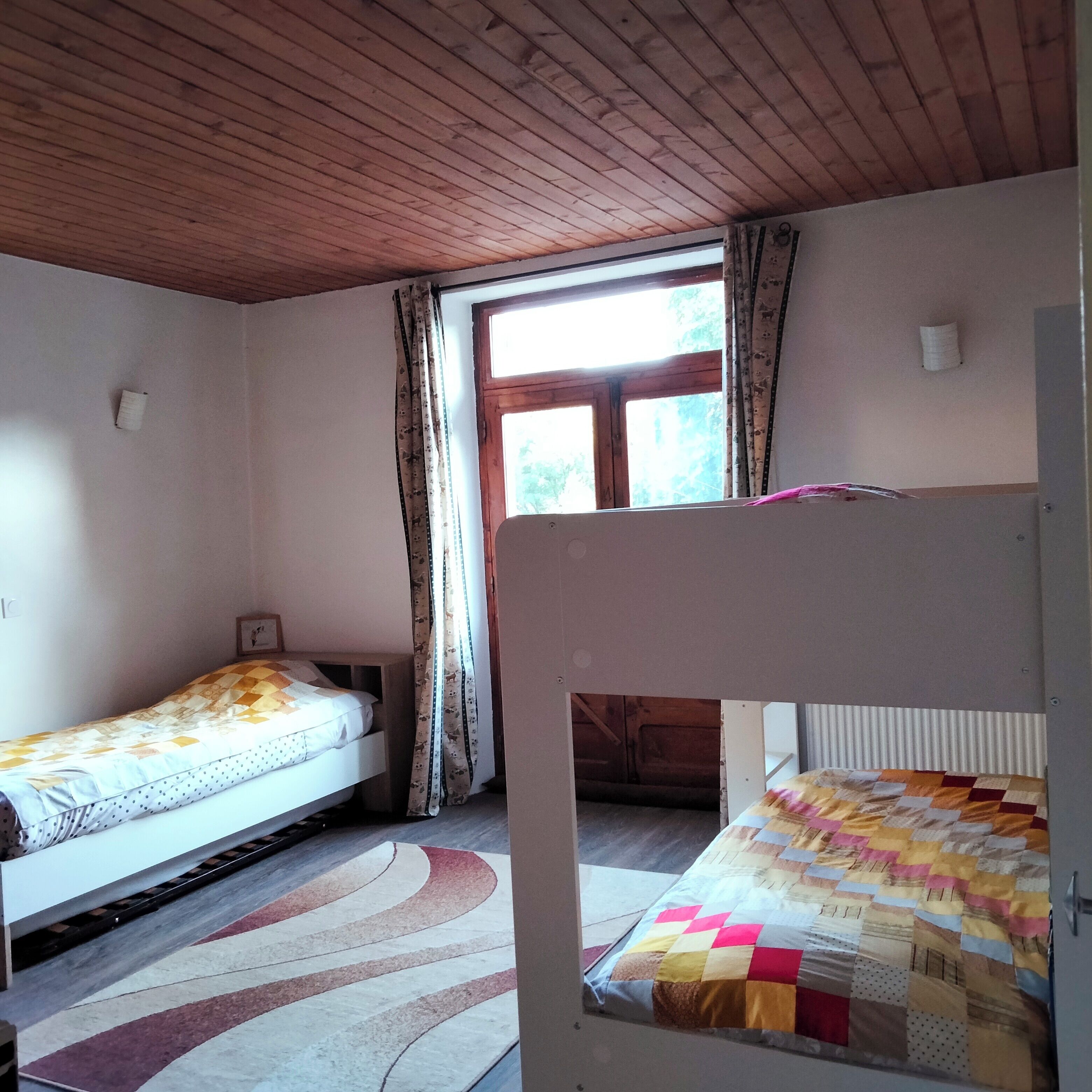 A room with two bunk beds, a window with curtains, and a patterned rug.