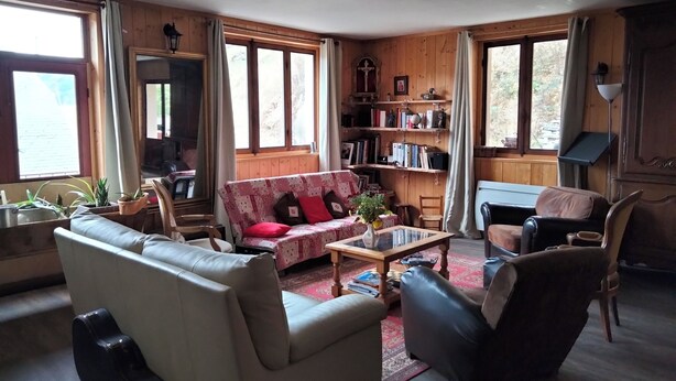 A cozy living room with a sofa, armchair, and coffee table. There is a bookshelf filled with books and decorative items. - Savoie, St François Longchamp, Très Grand Appartement de 180 m2, 12 Couchages (Saint-François-Longchamp)