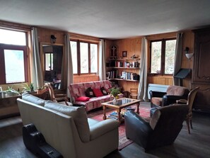 Un salon chaleureux avec un canapé, un fauteuil et une table basse. On y trouve une bibliothèque remplie de livres et d’objets décoratifs.
