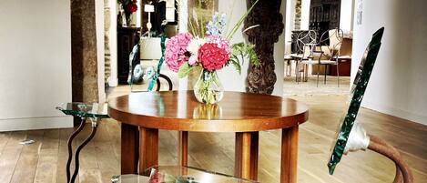 A round wooden table with a glass top, surrounded by chairs with metal frames. A vase with flowers is placed on the table.