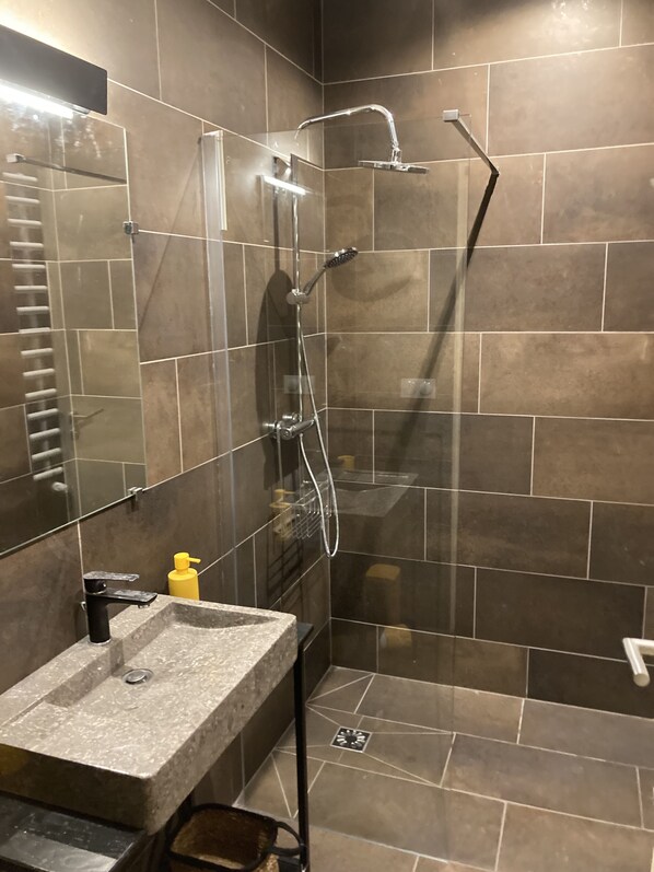 A modern bathroom with a glass-enclosed shower, a granite sink, and a mirror.