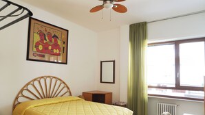 A room with a bed, a ceiling fan, a window with curtains, a radiator, and a framed picture on the wall.