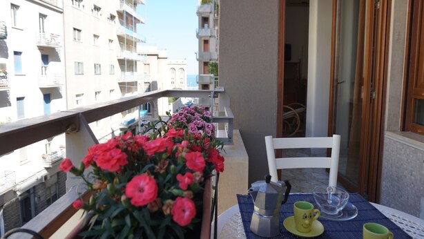A balcony with a table set for two, a chair, and a potted plant with flowers.
