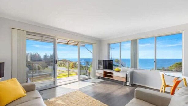 Een moderne woonkamer met een grote schuifpui die uitkomt op een balkon met uitzicht op de oceaan.