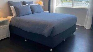 Een slaapkamer met een bed, nachtkastje, plafondventilator en een raam met uitzicht.