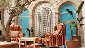 Un rincón acogedor con sillones estampados y una mesita pequeña, frente a puertas azules y detalles de azulejos ornamentales.