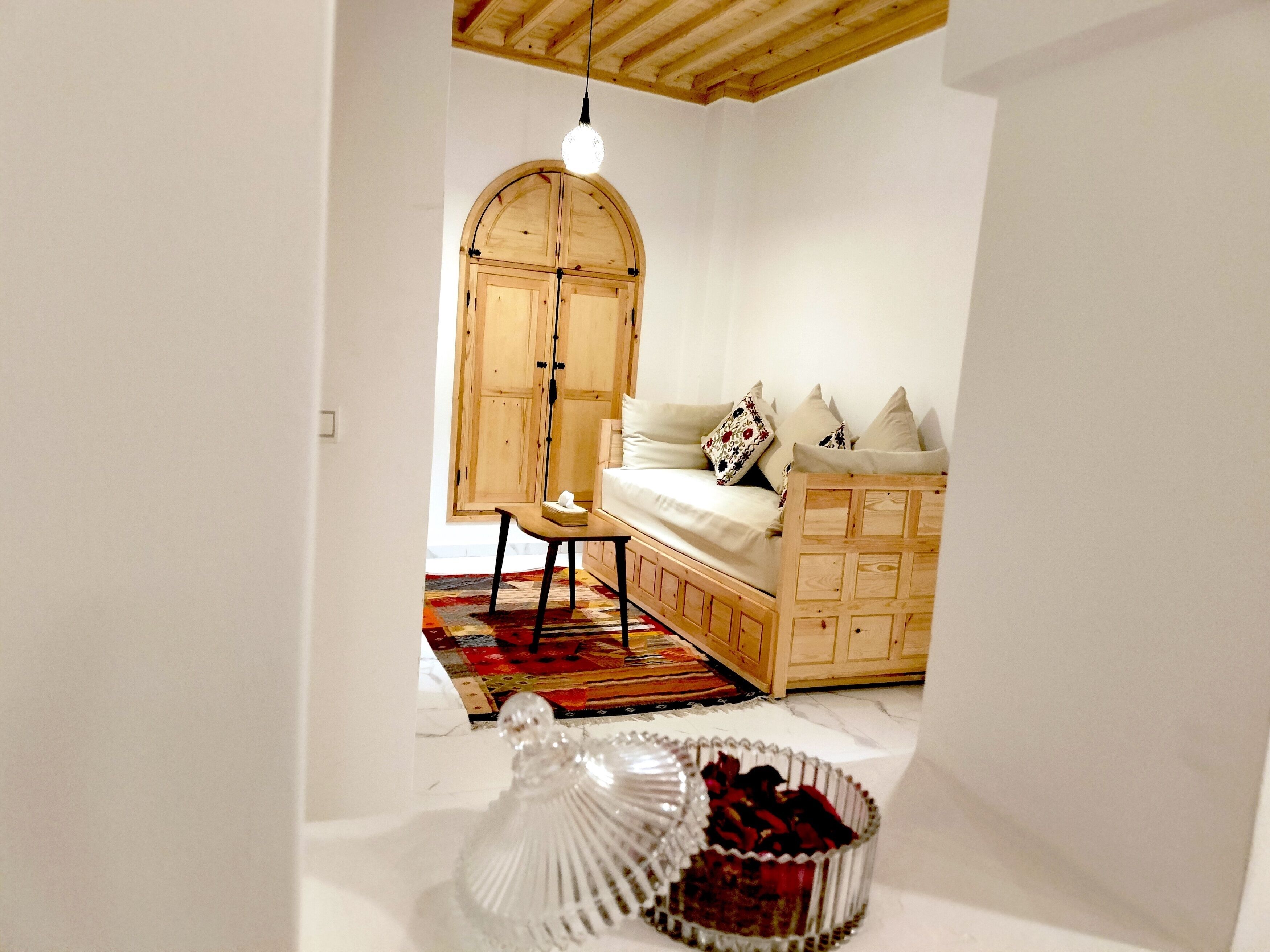 Un dormitorio acogedor con un armario de madera, una cama con almohadas, una mesita pequeña y un cuenco de vidrio decorativo en el suelo.