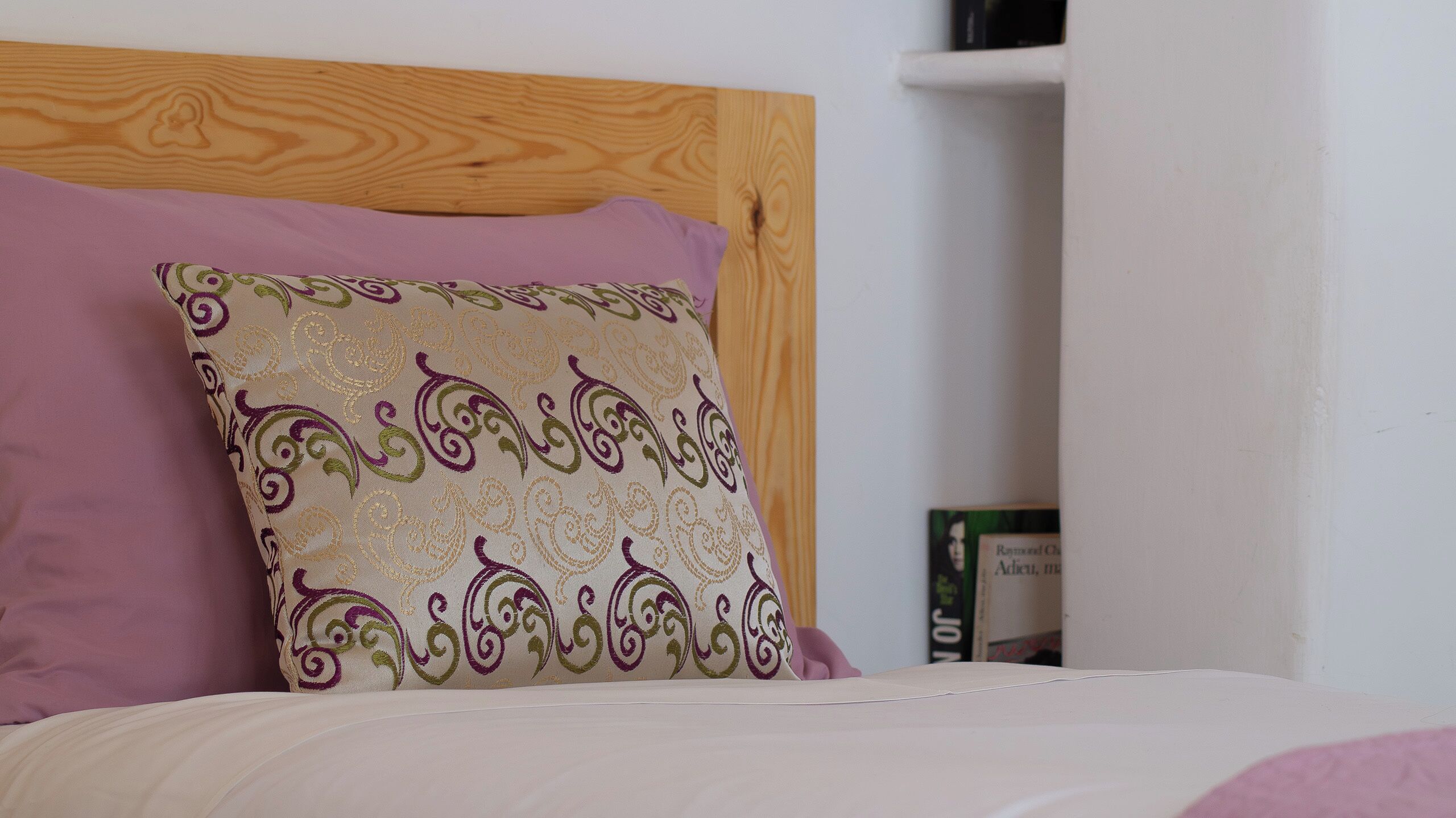 A bed with a wooden headboard, a purple pillow, and a patterned pillow.