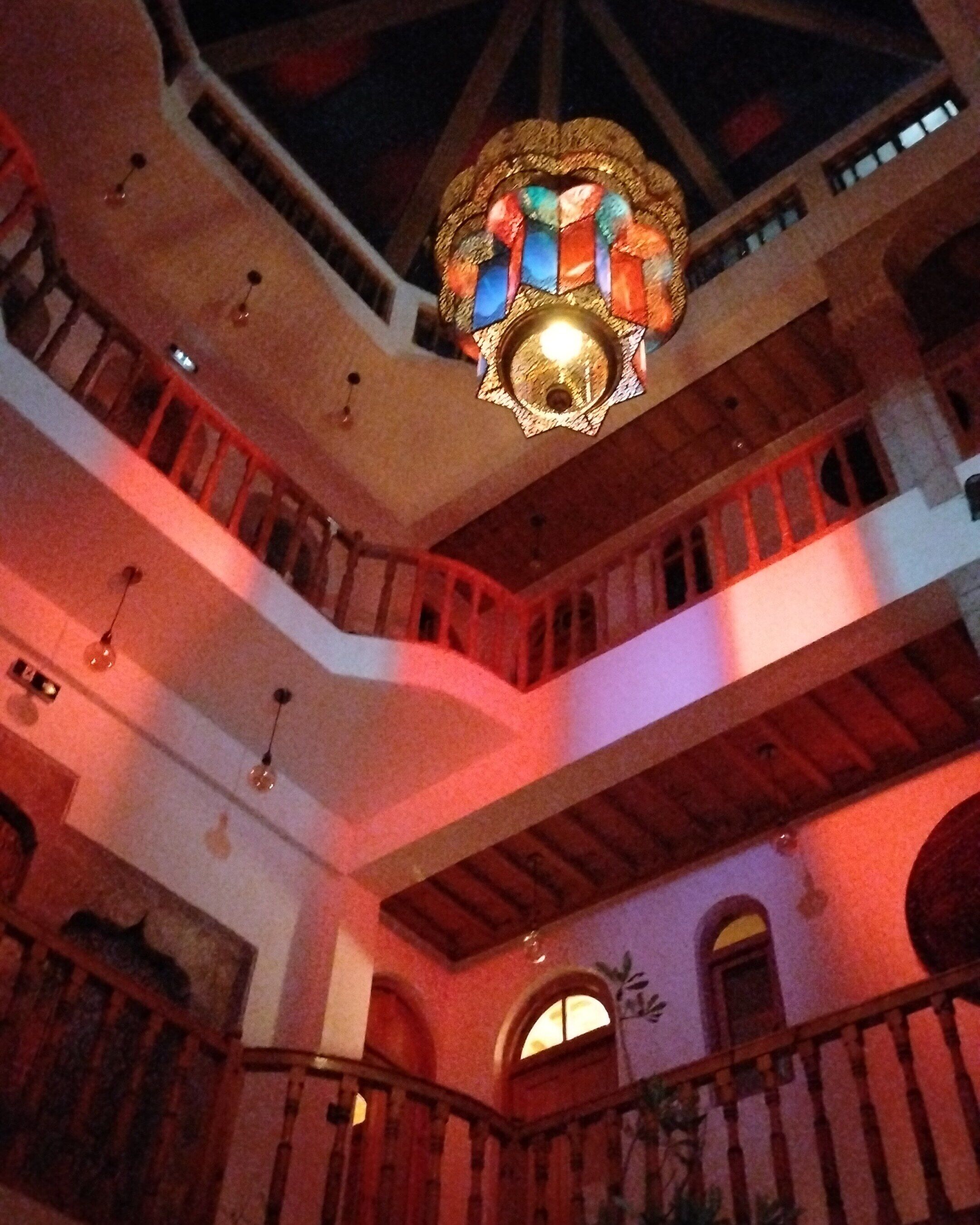 A multi-level interior with a central chandelier, wooden balconies, and arched doorways.