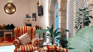 Una sala de estar con un sofá estampado, plantas verdes grandes y una pared decorativa.