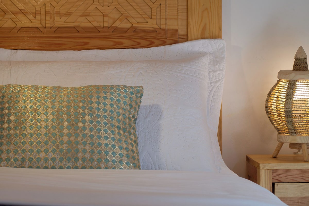 A bed with a patterned pillow, a wooden headboard, and a bedside lamp.