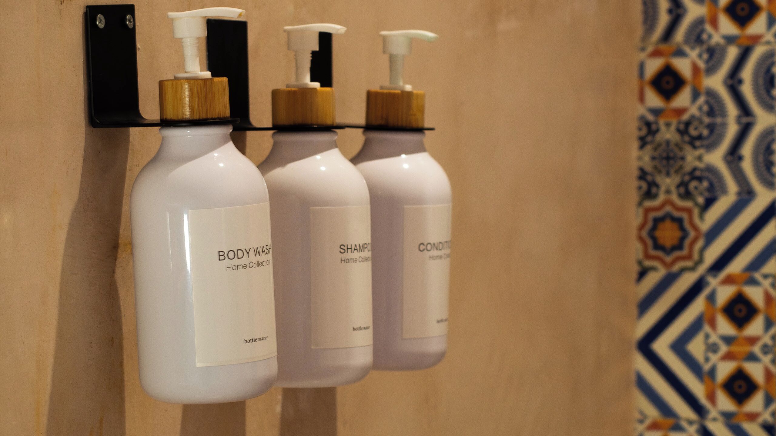 Three bottles of body wash, shampoo, and conditioner hanging on a wall.