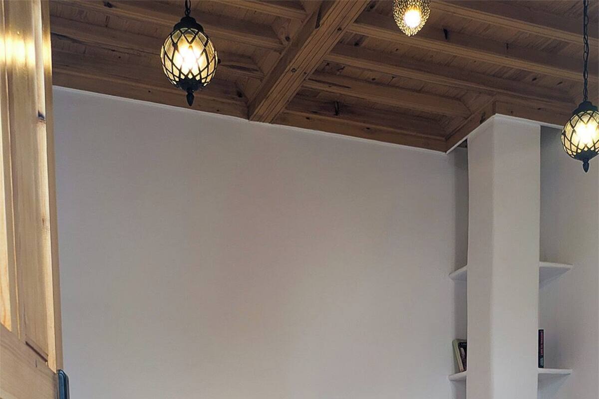 A bedroom with two beds, wooden headboards, a white wall, a bookshelf, and hanging pendant lights.