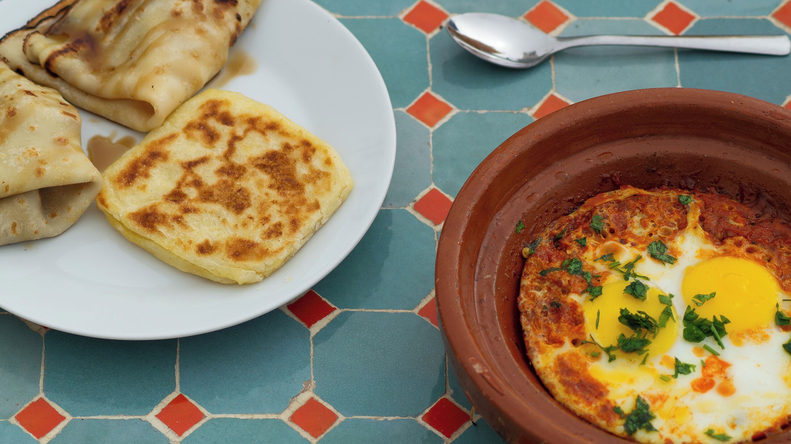 A plate of food with two pieces of flatbread and a bowl of shakshuka with an egg.
