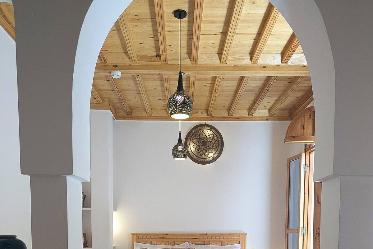 A bedroom with a wooden bed, a patterned rug, a ceiling fan, and a wall-mounted decorative plate.