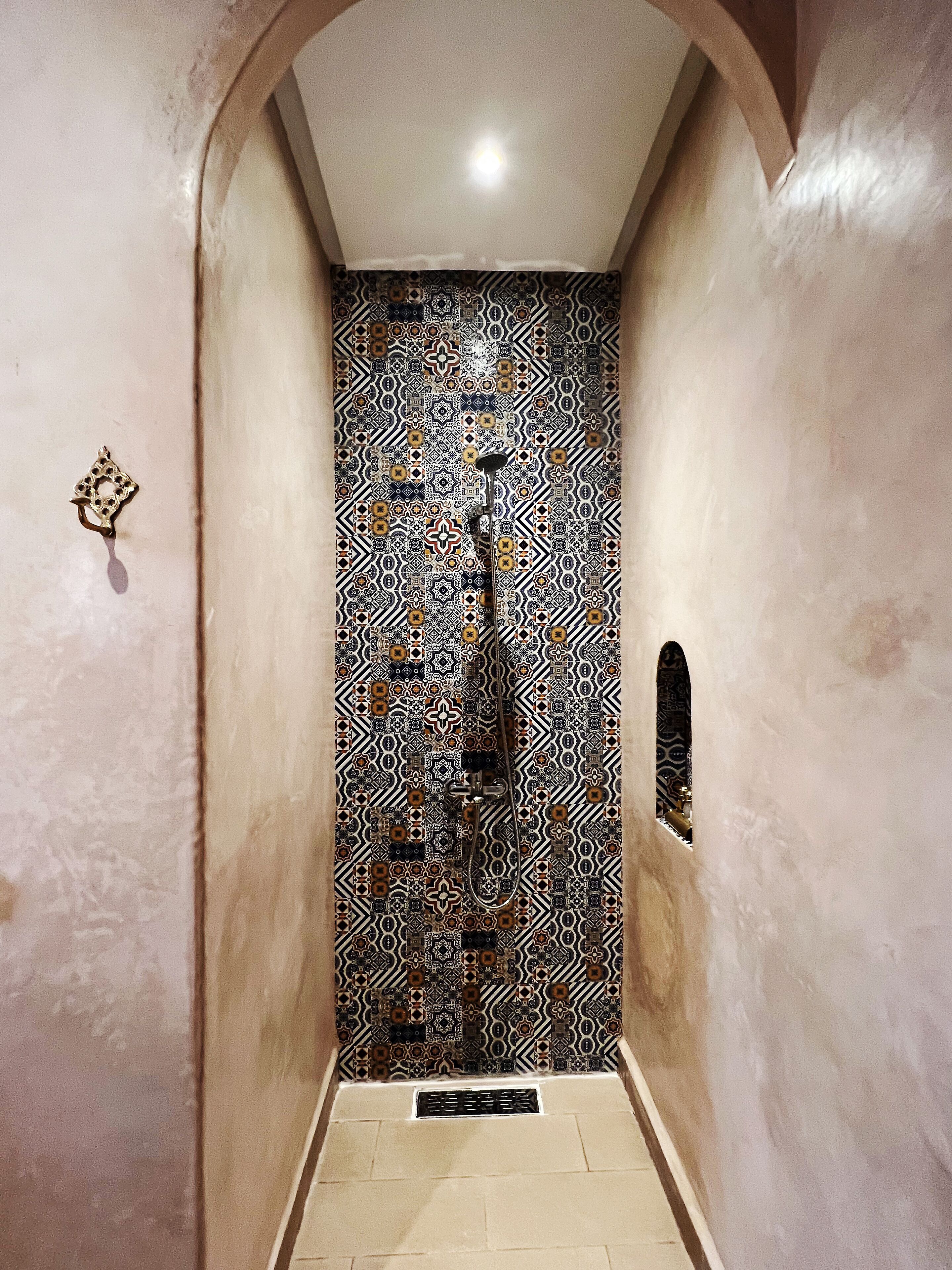 A narrow hallway with patterned walls, a metal door, and a small window.