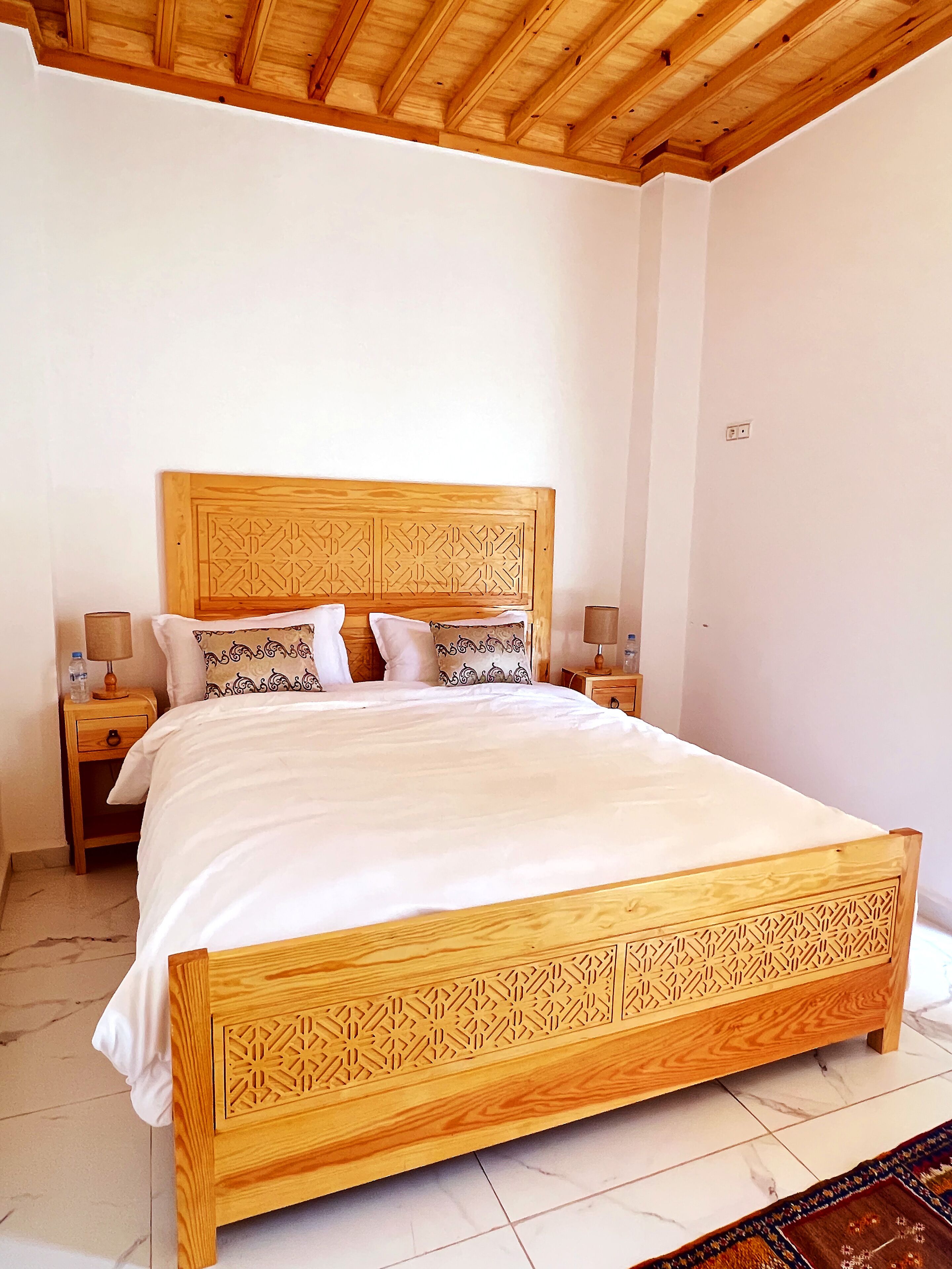 A large bed with a wooden headboard and footboard, two bedside tables, and a patterned rug.