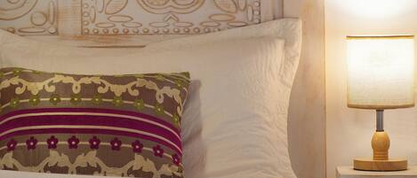A neatly made bed with a patterned pillow, a white headboard, and a bedside lamp on a wooden nightstand.