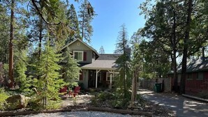 A house surrounded by trees, with a gravel driveway and a red chair in the yard. - Adventure Awaits! - Twain Harte Getaway (Twain Harte)