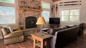 A cozy living room with a stone fireplace, leather furniture, and ski equipment on the wall. - Adventure Awaits! - Twain Harte Getaway (Twain Harte)