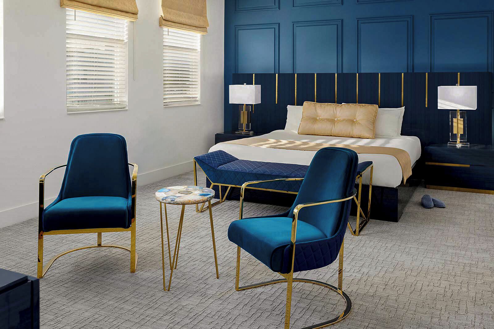 Una habitación de hotel con una cama grande, dos sillones, una mesita redonda y dos lámparas de noche.
