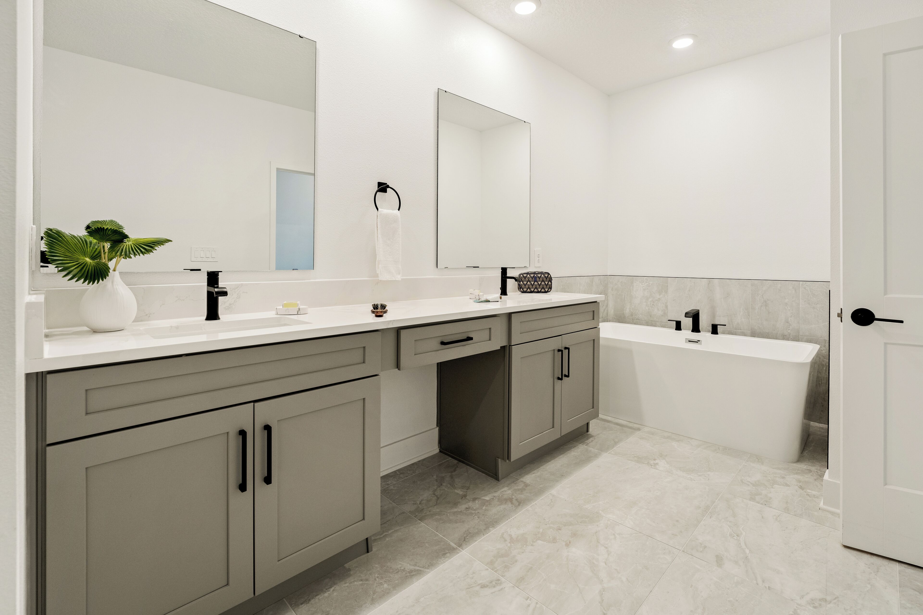 A modern bathroom with a white sink, a large mirror, a bathtub, and grey cabinets.