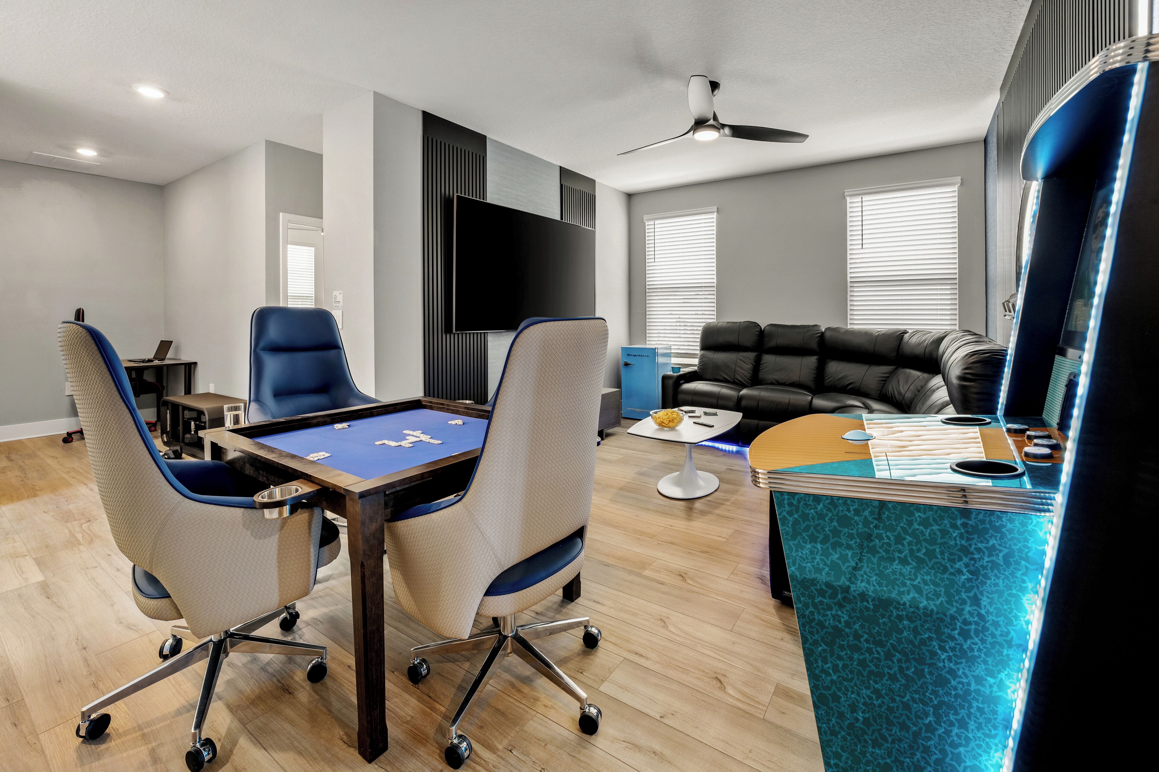 A modern living room with a pool table, comfortable seating, a flat-screen TV, and a ceiling fan.