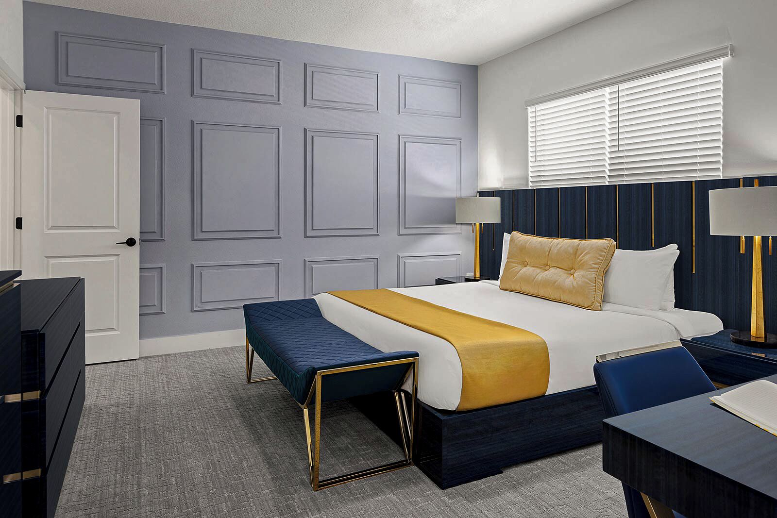 A hotel room with a bed, bedside tables, a bench, a dresser, and a window with blinds.