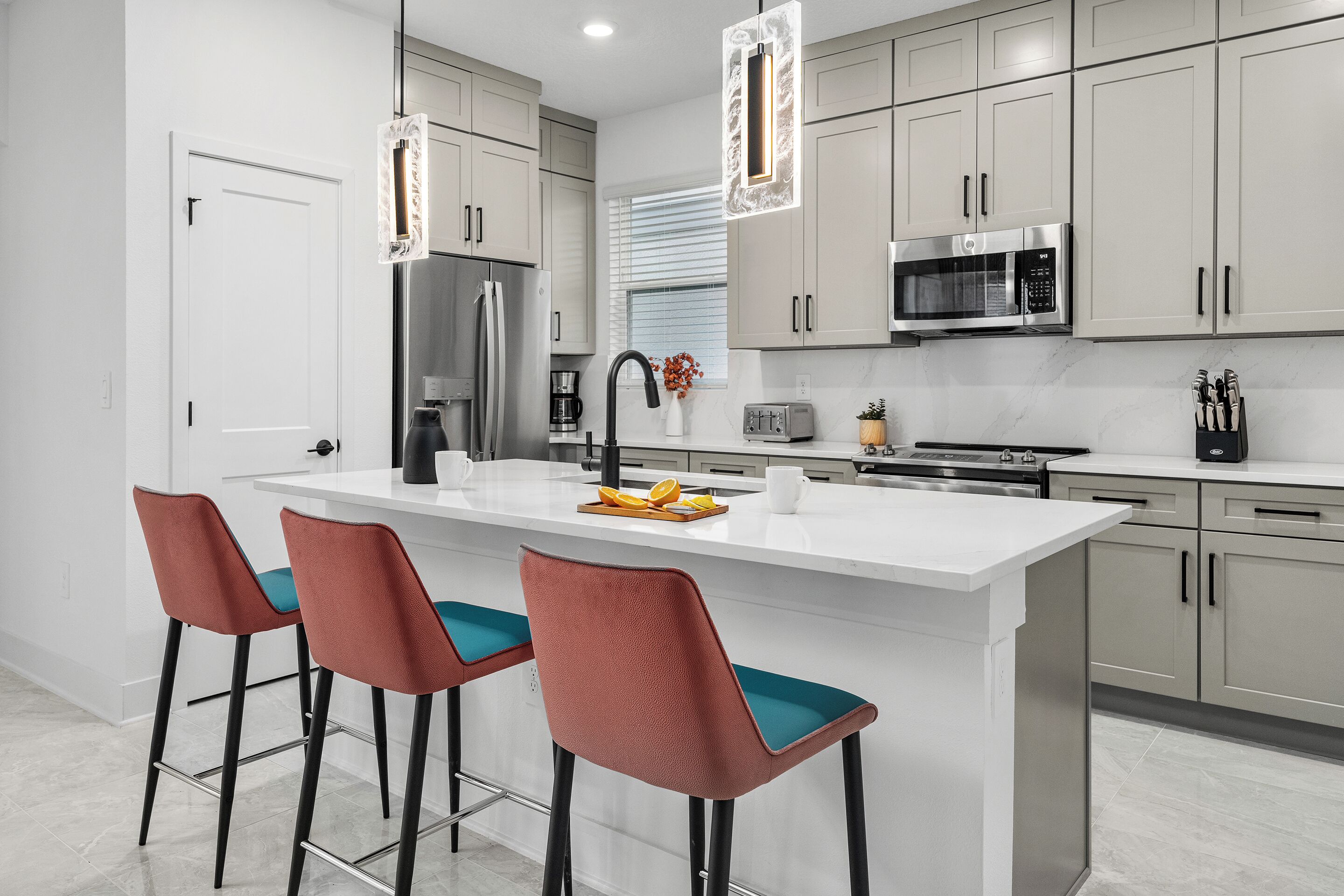 Cozinha moderna com ilha central, banquetas, eletrodomésticos de aço inoxidável e armários em tons claros.