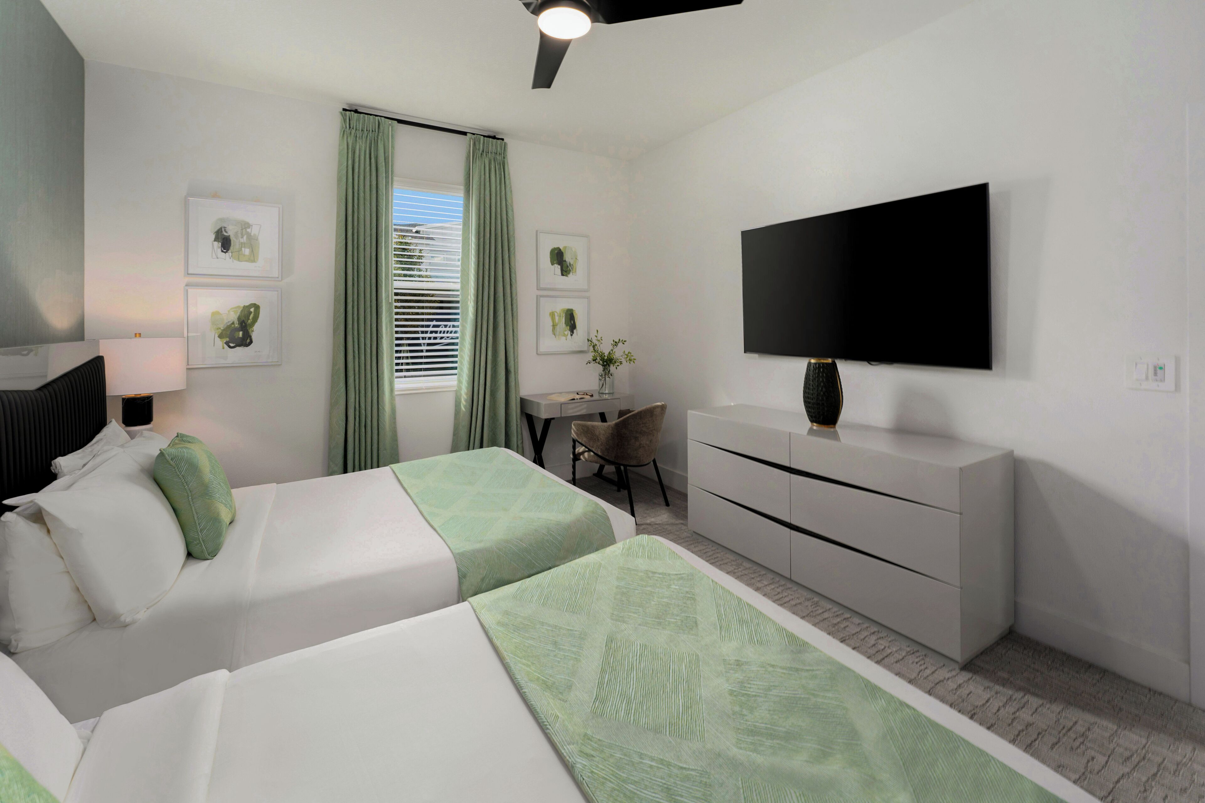 A hotel room with two beds, a desk, a chair, a TV, and artwork on the walls.