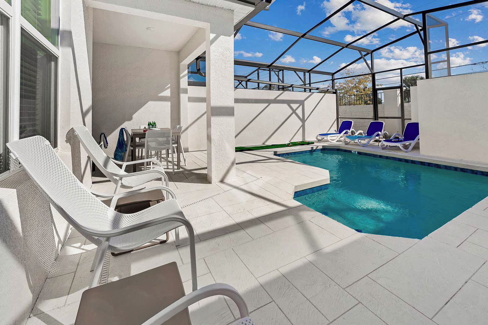 An indoor swimming pool with clear blue water, surrounded by white tiled flooring and white lounge chairs.