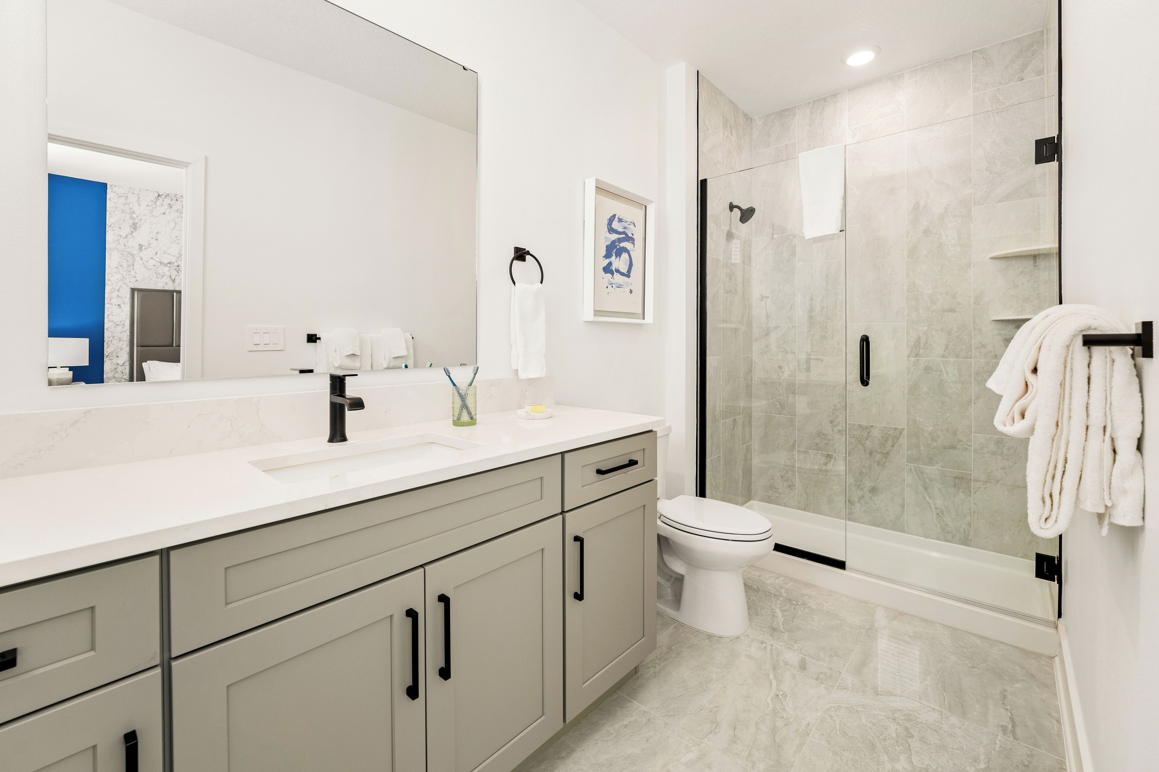 A modern bathroom with a large mirror, a sink, a toilet, and a shower area.