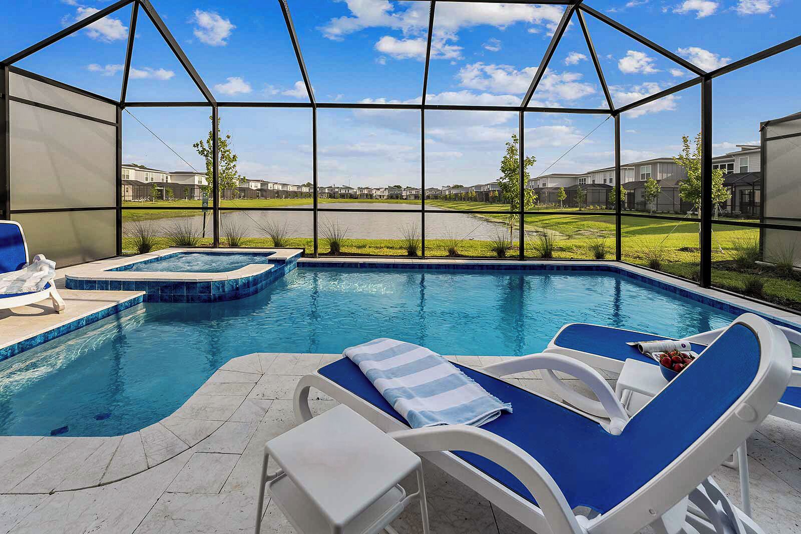 A swimming pool with lounge chairs and a hot tub, surrounded by a covered area with a view of houses in the background.