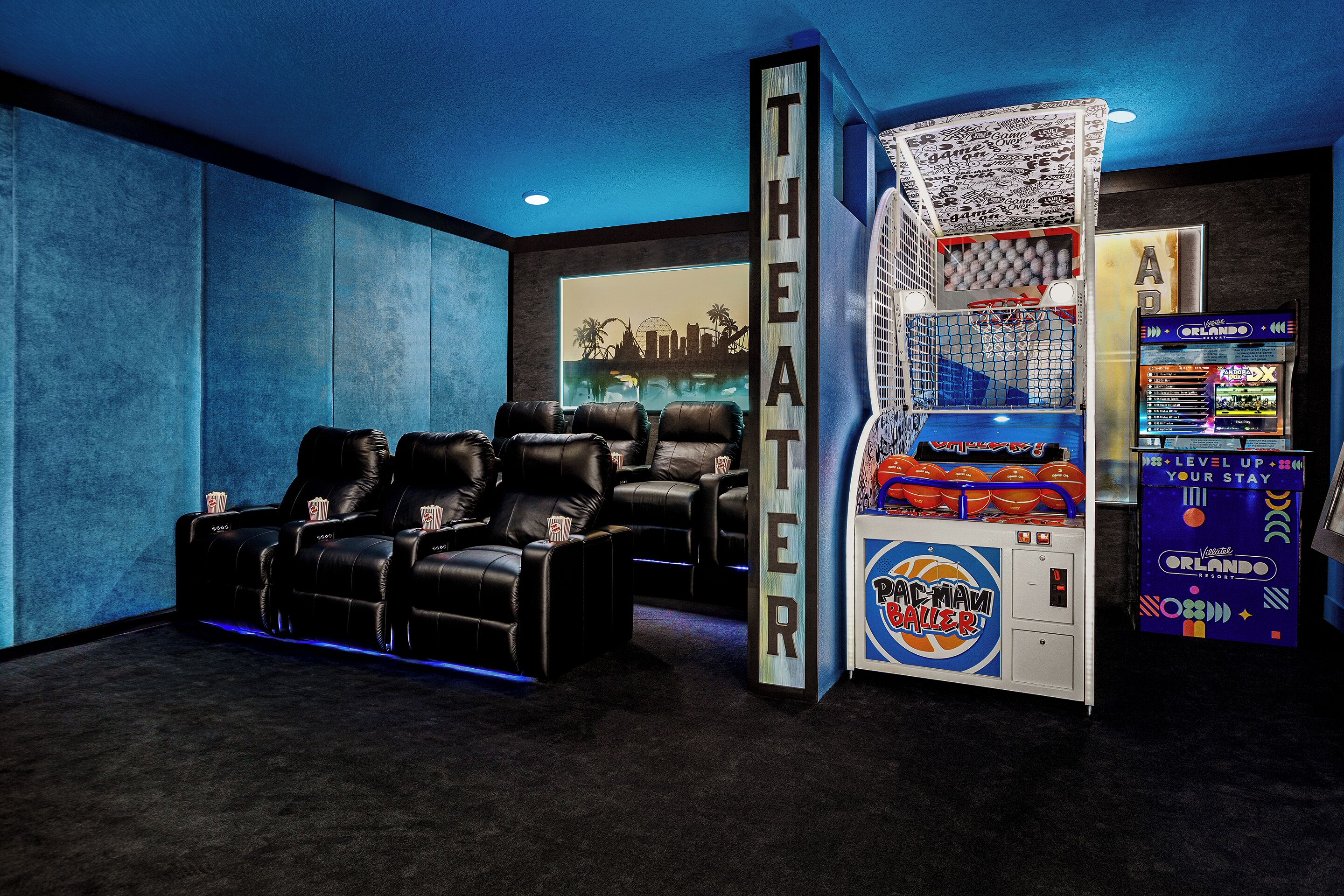 Una sala de cine en casa con sillones de cuero reclinables, una pantalla grande y una máquina de videojuegos Pac-Man.