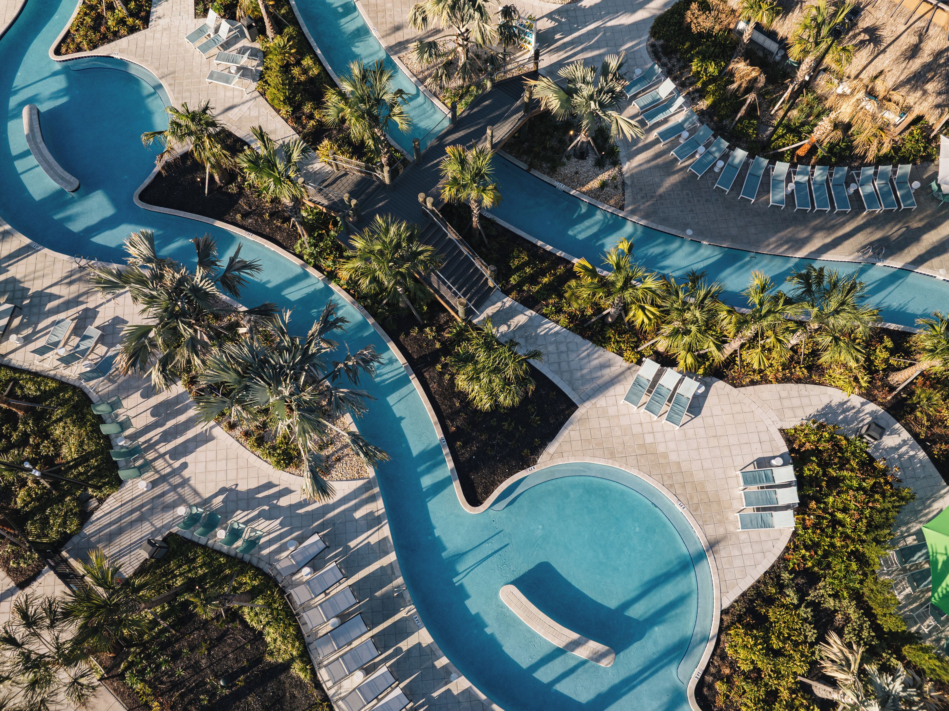 An aerial view of a resort with multiple swimming pools, sun loungers, and palm trees.