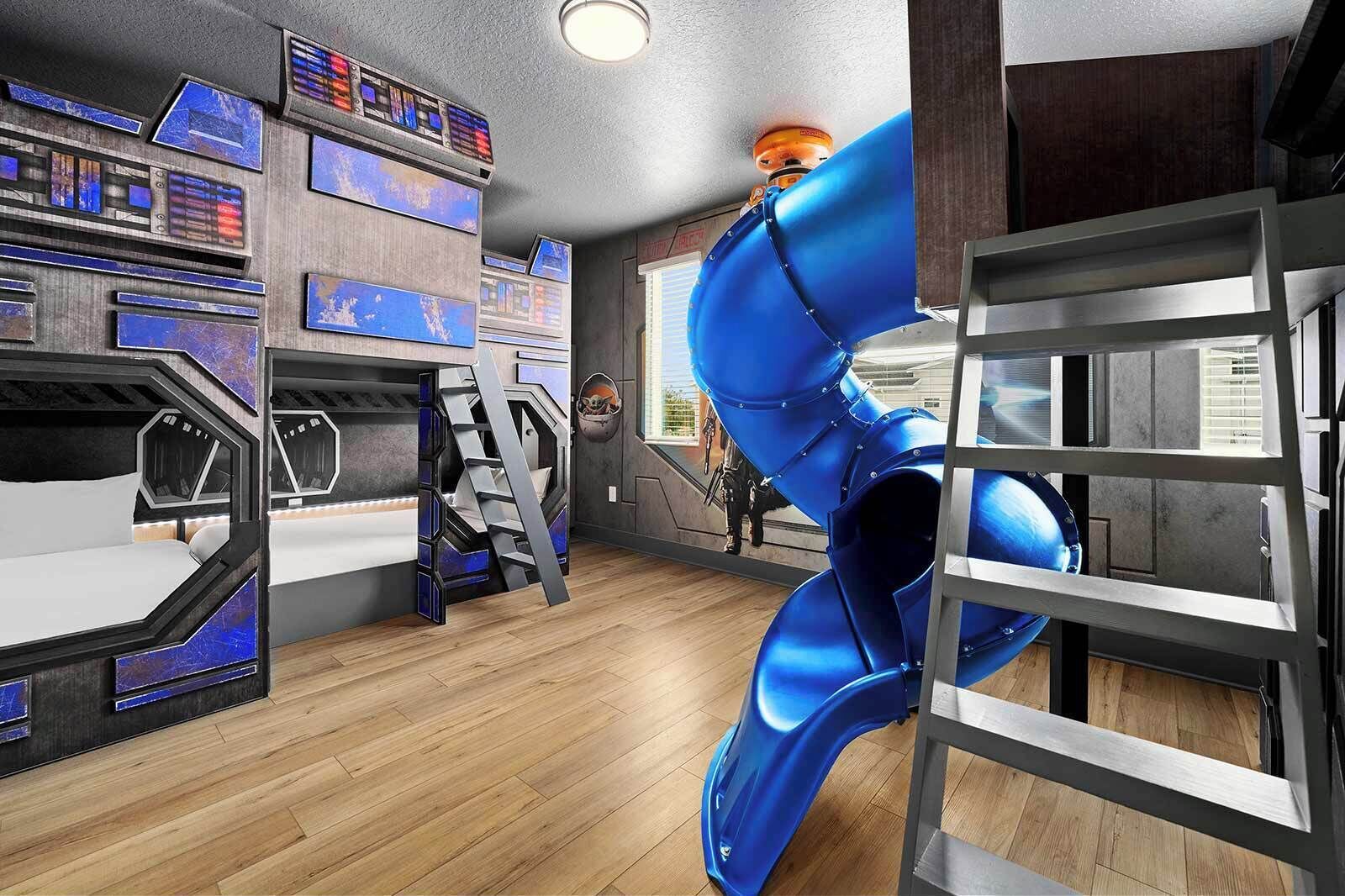Une salle de jeux pour enfants avec des lits superposés, un toboggan et un mur équipé d’écrans.