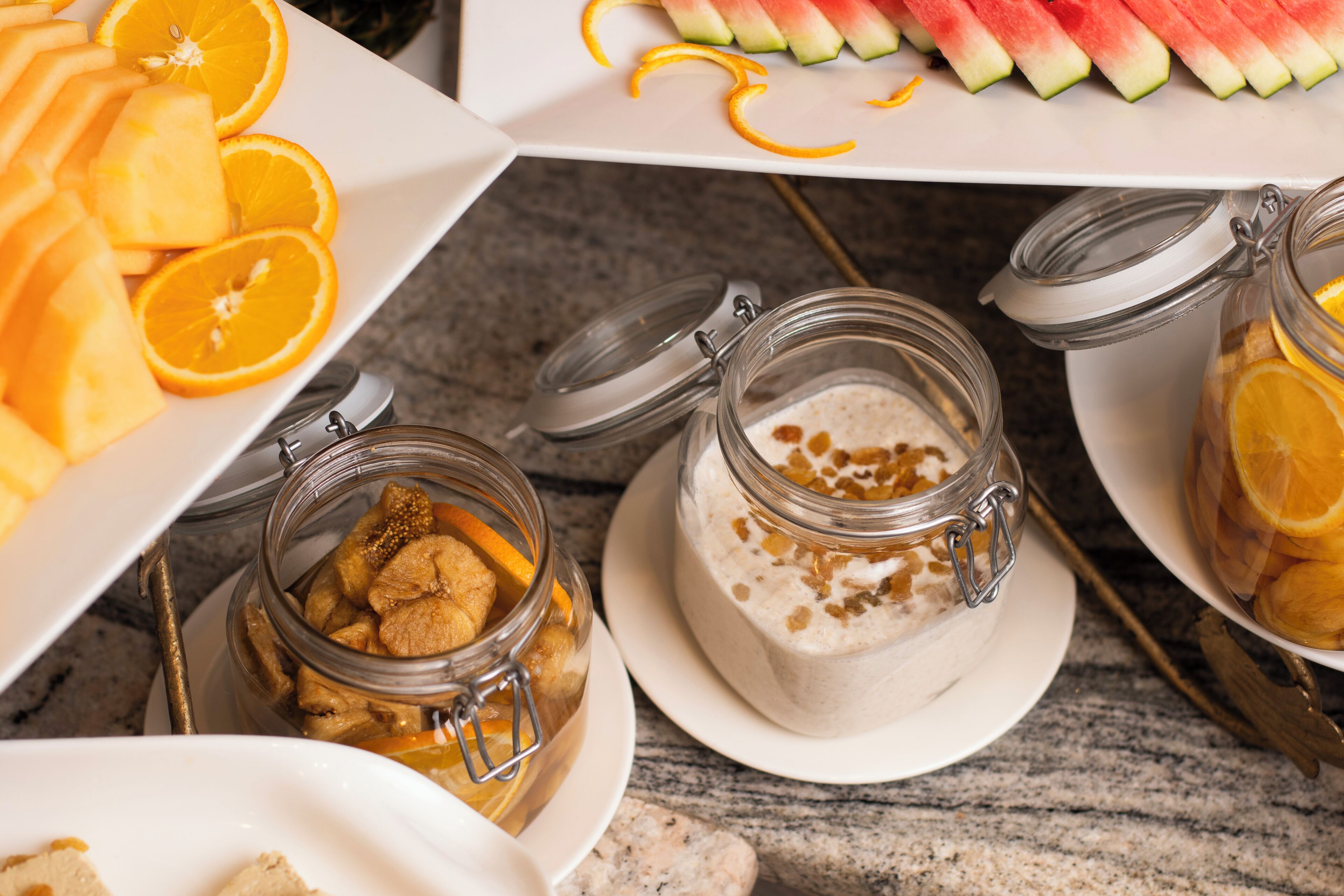 A buffet with various food items including sliced oranges, watermelon, and jars of food.